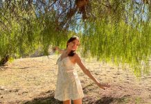 A girl in a flowy summer dress dances under a tree.