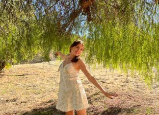 A girl in a flowy summer dress dances under a tree.