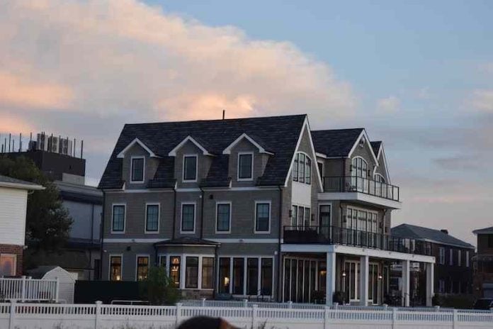 A dark beige three-story house with big windows, two balconies, and white pillars