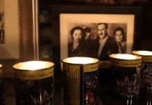 Four lit remembrance candles sit in front of a framed sepia-toned photo of a family.