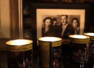 Four lit remembrance candles sit in front of a framed sepia-toned photo of a family.