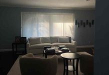 An dark, empty living room of white furniture with drawn blinds.