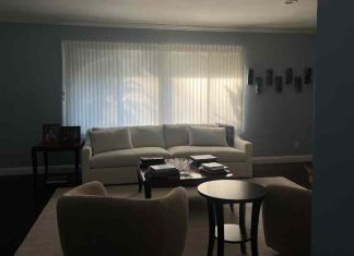 An dark, empty living room of white furniture with drawn blinds.