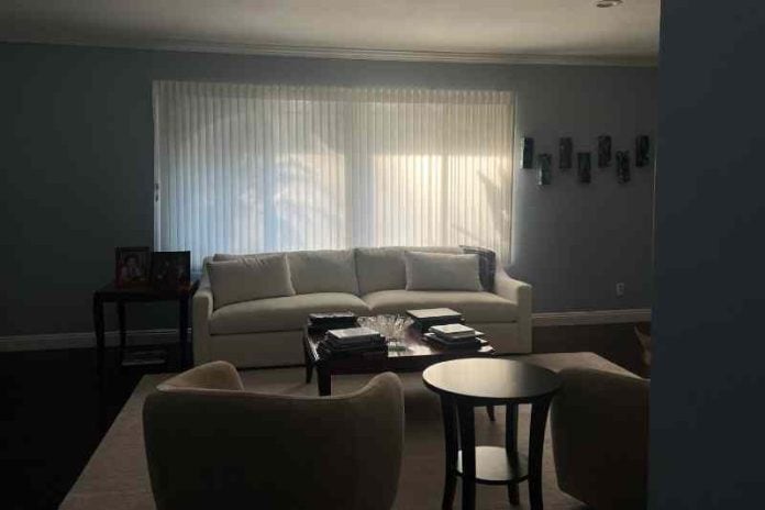An dark, empty living room of white furniture with drawn blinds.