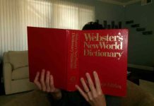 Woman reads the Webster's New World Dictionary, blocking her face with the large red book.