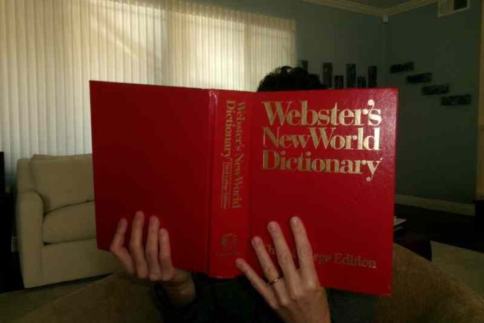Woman reads the Webster's New World Dictionary, blocking her face with the large red book.