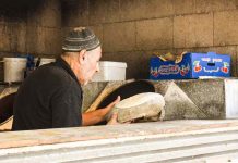 A middle-aged man wearing a kippah places pita dough to go into a stone oven.