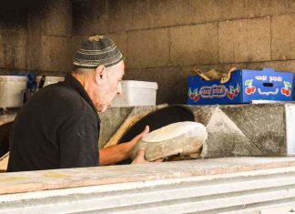 A middle-aged man wearing a kippah places pita dough to go into a stone oven.
