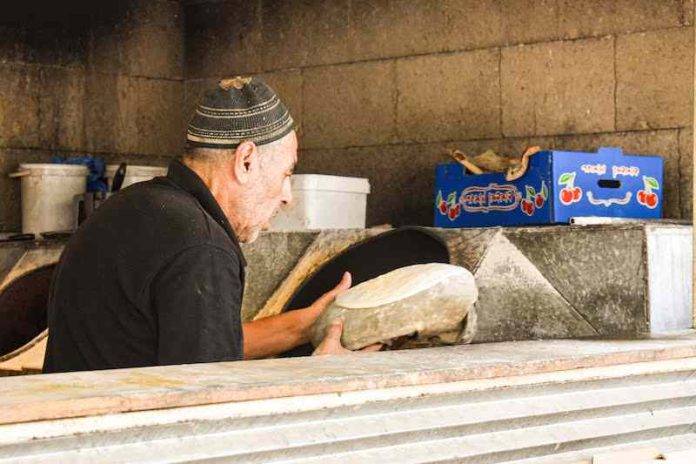 A middle-aged man wearing a kippah places pita dough to go into a stone oven.