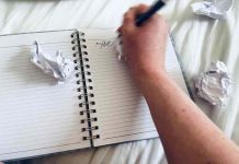 A hand scribbles in a notebook surrounded by crumpled-up pieces of paper.