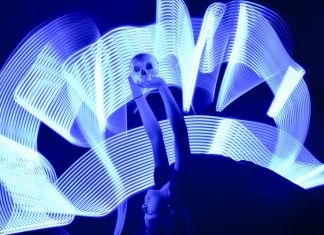 A girl arches backward, holding a skull aloft over her head. Waves of white light surround her.