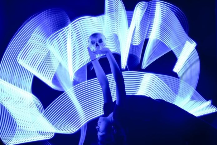 A girl arches backward, holding a skull aloft over her head. Waves of white light surround her.