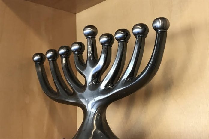A silver chanukiah rests on a wooden shelf.