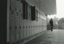 A boy dressed in a black hoodie stands on an outdoor balcony in front of a row of open lockers.
