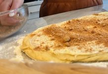 Next to a large piece of dough dusted with crumbs, hands reach into a mixing bowl full of graham cracker pieces.