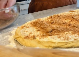 Next to a large piece of dough dusted with crumbs, hands reach into a mixing bowl full of graham cracker pieces.
