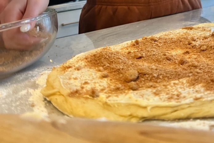 Next to a large piece of dough dusted with crumbs, hands reach into a mixing bowl full of graham cracker pieces.