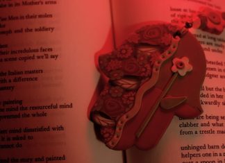 Red-tinted photograph of a clay hamsa atop an open book of poetry