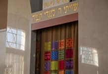 A synagogue ark with colorful tapestry curtains and Hebrew inscriptions.