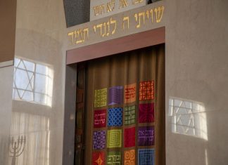 A synagogue ark with colorful tapestry curtains and Hebrew inscriptions.