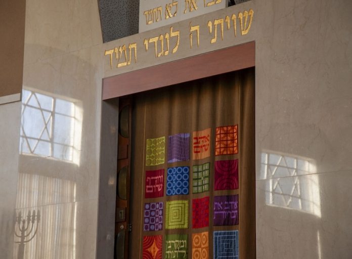 A synagogue ark with colorful tapestry curtains and Hebrew inscriptions.