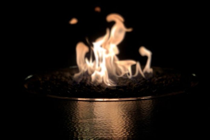 A fire burns in a bronze vessel against a black background.