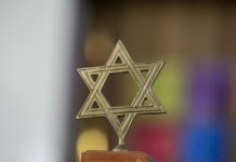 A brass Jewish star stands on a wooden base against a blurred background.