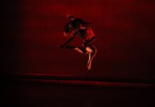 A dancer mid-leap beneath moody red stage lights.