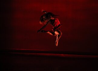 A dancer mid-leap beneath moody red stage lights.
