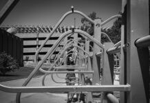 A triangular bike rack dominates the foreground of the photo, framing the smiling face of a teen girl who peers through them.