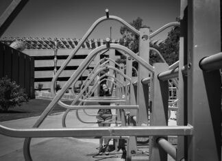 A triangular bike rack dominates the foreground of the photo, framing the smiling face of a teen girl who peers through them.