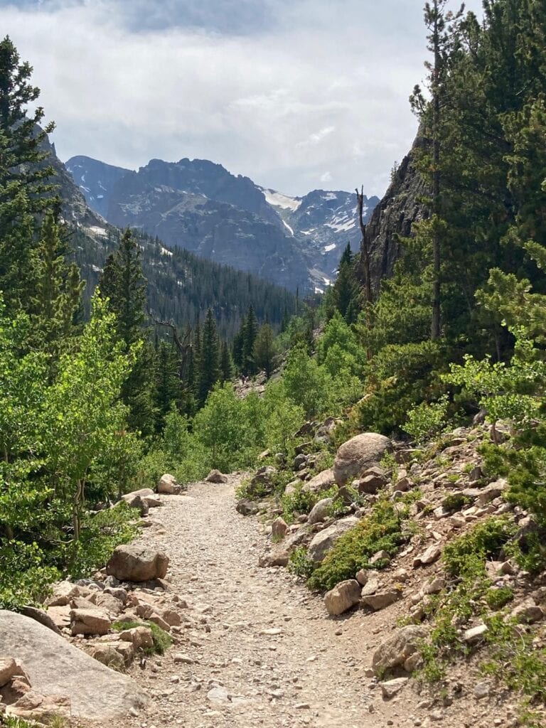 A tree-lined Colorado trail in a rocky valley with mountains in the middle distance