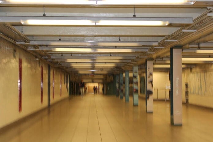 A slightly blurry scene of a well-lit, beige walled, underground station.