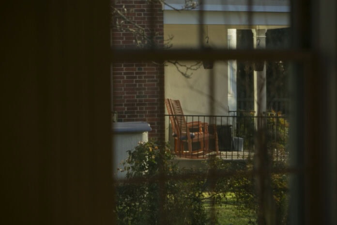 Framed in Beauty Gazing through a window, we look out on a porch with two rocking chairs, framed by greenery.