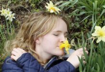 A young woman lying in the grass, smelling a yellow flower