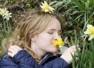 A young woman lying in the grass, smelling a yellow flower