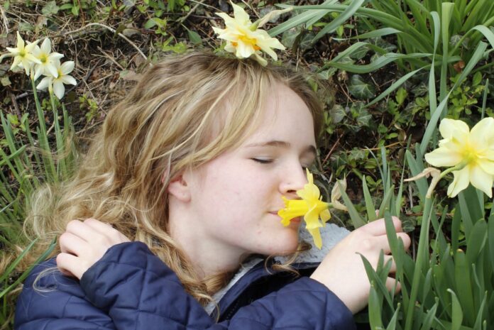 A young woman lying in the grass, smelling a yellow flower