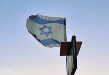 Over the Atlantic A tattered Israeli flag flies on a post against a pale blue sky.