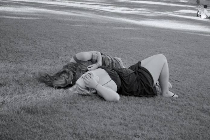 Black and white photo of two girls lying on the grass, laughing.