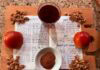 On a cutting board, there is a Haggadah open to "The Four Sons" section. It is surrounded by a cut apple, a cup of wine, a bowl of cinnamon, and walnuts.