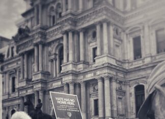 A crowd of people in front of a stately building in Philadelphia. One person holds up a sign that says "Hate Has No Home Here."