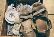 A pair of brown leather sandals, stained with wear, sit atop a wooden crate filled with antique objects.