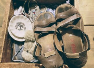 A pair of brown leather sandals, stained with wear, sit atop a wooden crate filled with antique objects.