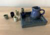 Naama Raun's Kiddush set includes a blue pitcher with five small individual cups. The pitcher and one of the individual cups sits on a ceramic tray decorated with floral print.