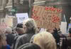 Winter Protesters march near a cardboard sign that says "Migration is an act of courage" surrounded by monarch butterflies.