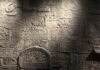 Eichah? Light streaks across a stone wall covered in Hebrew text and Jewish symbols with streaks.
