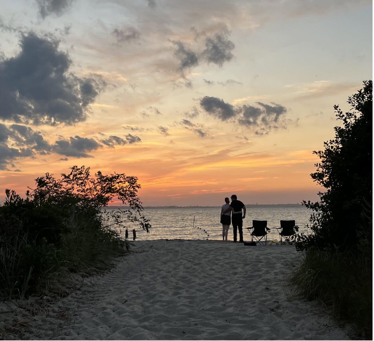A couple embraces on a sandy beach while watching the sun set over the water in Seaside Park, New Jersey.
