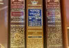 A close-up of three siddurim (Jewish prayer books) in shades of red and brown with gold-foiled Hebrew letters on the spine.