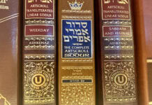 A close-up of three siddurim (Jewish prayer books) in shades of red and brown with gold-foiled Hebrew letters on the spine.