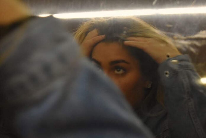 Anxiety 2 A teen girl is running her fingers through her hair while looking at her reflection in a slightly blurry mirror. Her arm covers one of her eyes and the bottom of her face, leaving only the top of her face visible.